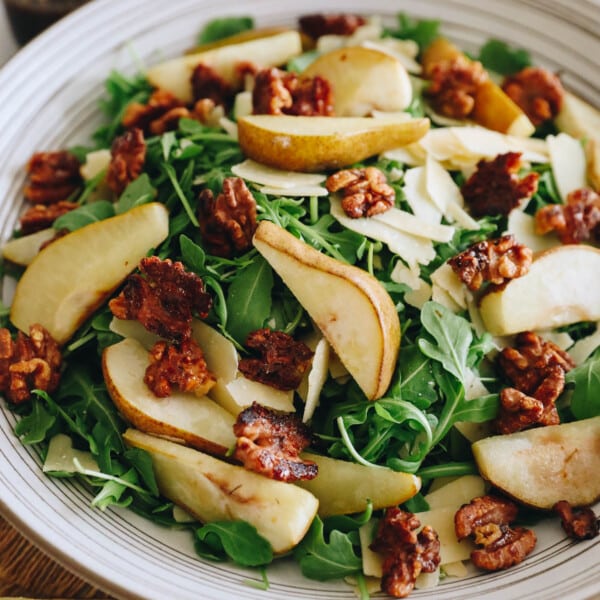 Roasted pear salad in a large white salad bowl with candied walnuts, parmesan and balsamic dressing.